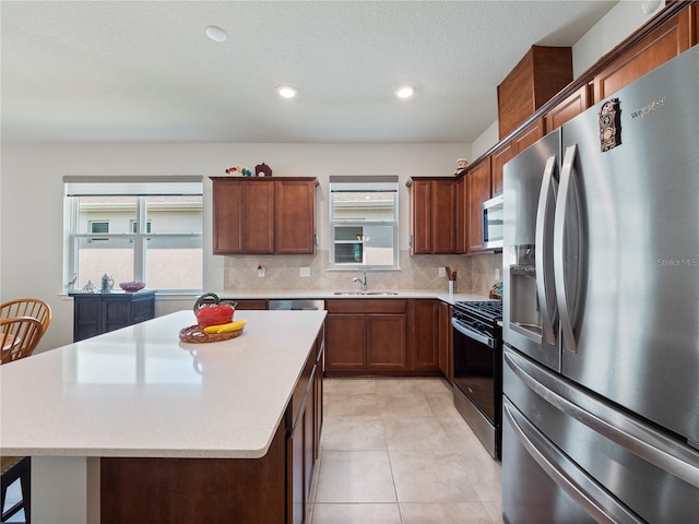 kitchen with a kitchen island, appliances with stainless steel finishes, backsplash, sink, and light tile floors