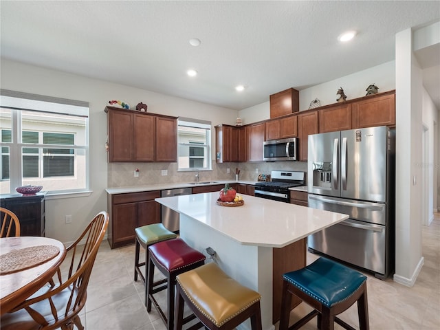 kitchen with backsplash, a kitchen island, light tile floors, sink, and appliances with stainless steel finishes