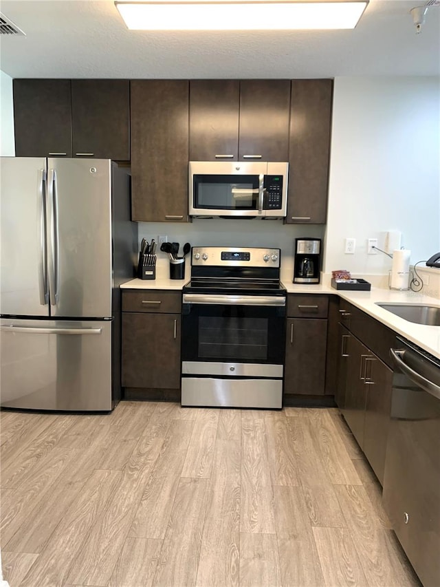 kitchen featuring dark brown cabinets, light hardwood / wood-style flooring, appliances with stainless steel finishes, and sink