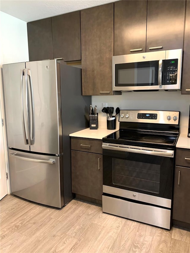 kitchen with dark brown cabinets, appliances with stainless steel finishes, and light wood-type flooring