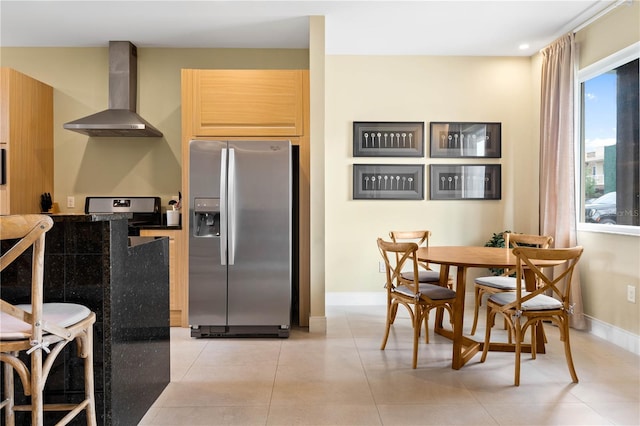 kitchen with light tile floors, range, wall chimney exhaust hood, light brown cabinets, and stainless steel refrigerator with ice dispenser