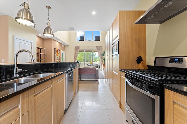 kitchen with light tile floors, wall chimney exhaust hood, appliances with stainless steel finishes, hanging light fixtures, and dark stone countertops