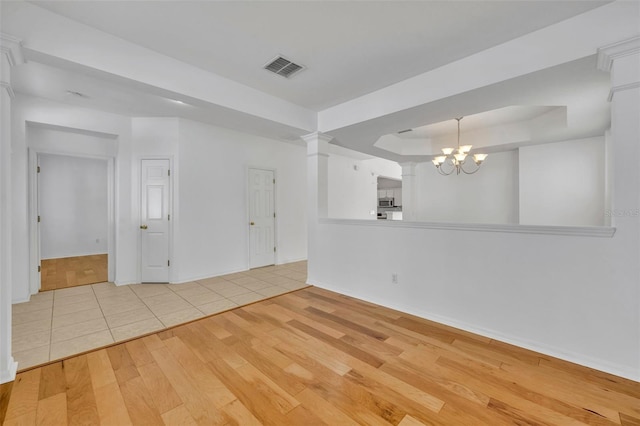 spare room featuring a raised ceiling, a chandelier, and light hardwood / wood-style floors