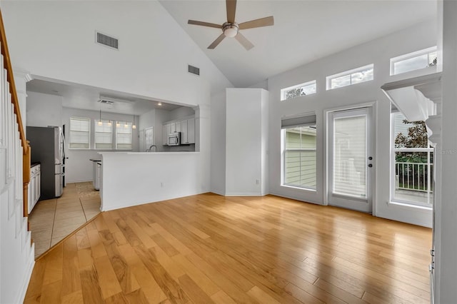 unfurnished living room featuring light wood-type flooring, high vaulted ceiling, ceiling fan, and a healthy amount of sunlight