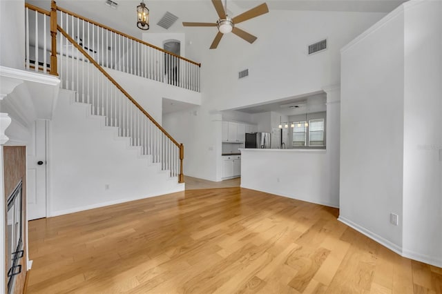 unfurnished living room featuring ceiling fan, light hardwood / wood-style flooring, and a towering ceiling