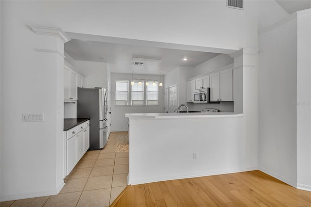 kitchen with light tile patterned flooring, kitchen peninsula, white cabinets, and stainless steel appliances