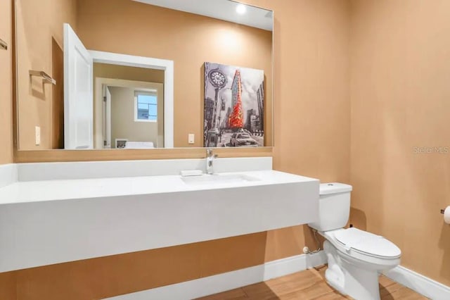 half bath with a sink, baseboards, toilet, and wood finished floors