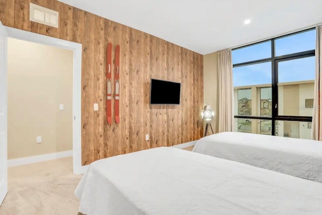 carpeted bedroom featuring a wall of windows, visible vents, baseboards, and wood walls