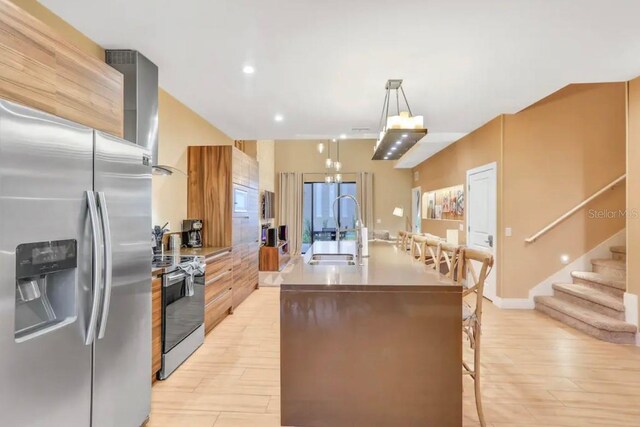 kitchen with light hardwood / wood-style flooring, hanging light fixtures, sink, a kitchen island with sink, and appliances with stainless steel finishes