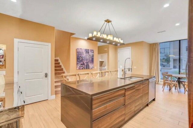 kitchen featuring light hardwood / wood-style floors, stainless steel dishwasher, decorative light fixtures, sink, and a kitchen island with sink