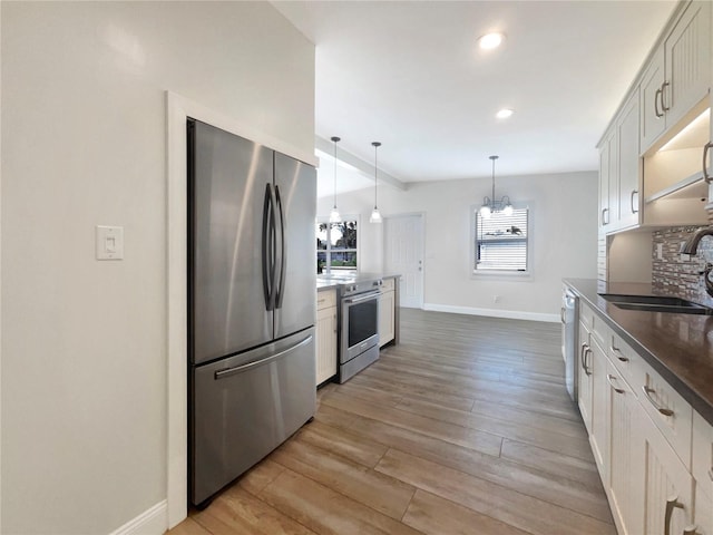 kitchen with appliances with stainless steel finishes, sink, light hardwood / wood-style flooring, white cabinets, and hanging light fixtures