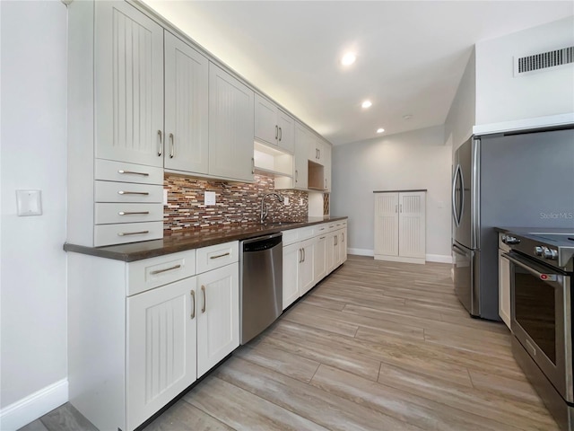 kitchen with white cabinetry, sink, stainless steel appliances, backsplash, and light wood-type flooring