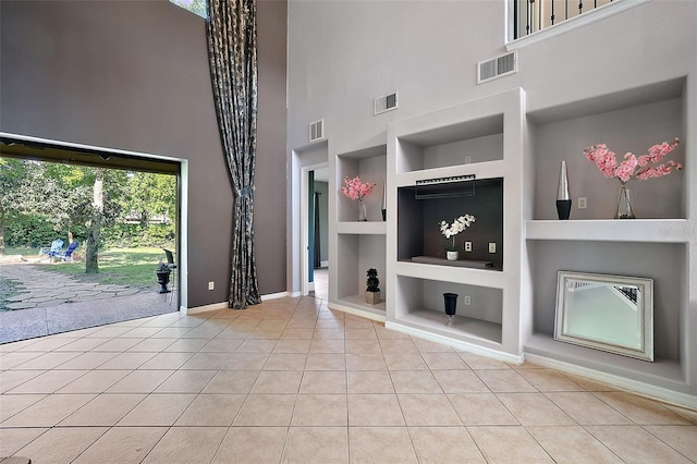 unfurnished living room with built in shelves, a towering ceiling, and light tile patterned floors