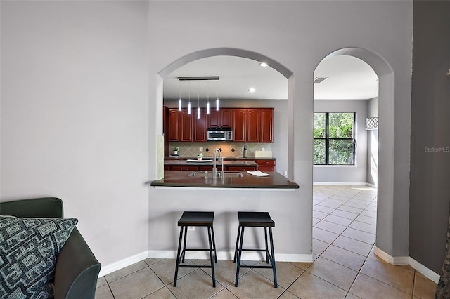 kitchen with decorative backsplash, kitchen peninsula, a breakfast bar, light tile patterned floors, and hanging light fixtures