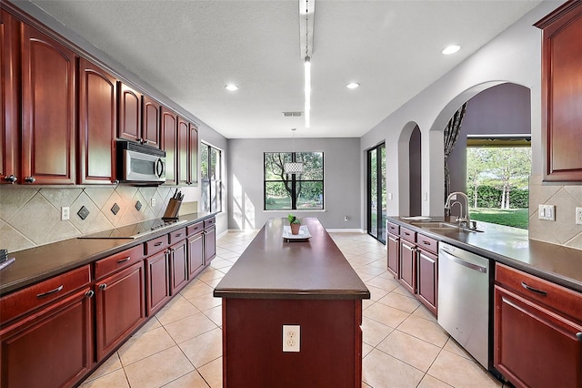 kitchen with appliances with stainless steel finishes, sink, light tile patterned floors, decorative light fixtures, and a center island