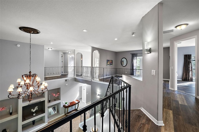 corridor featuring wood-type flooring, a textured ceiling, and an inviting chandelier