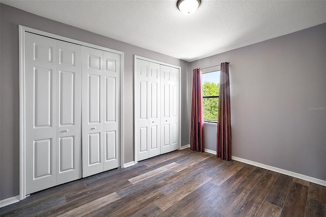 unfurnished bedroom featuring a textured ceiling, dark hardwood / wood-style flooring, and two closets