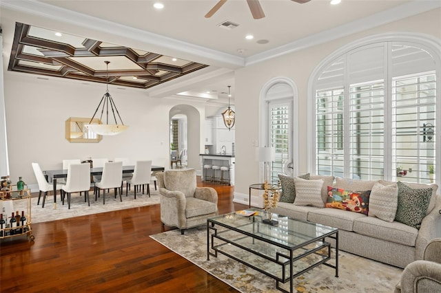 living room featuring beamed ceiling, coffered ceiling, ceiling fan with notable chandelier, light wood-type flooring, and crown molding