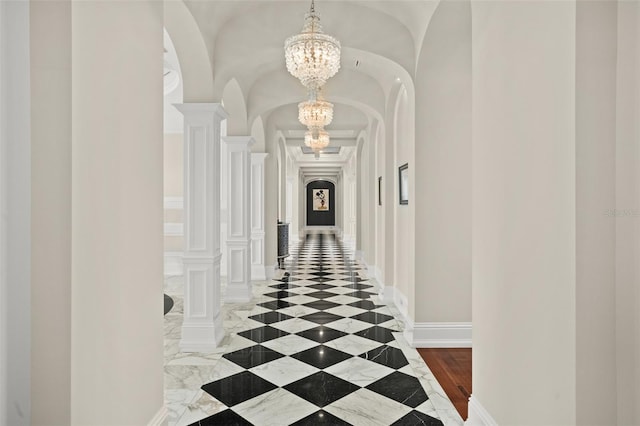 hall featuring dark tile flooring, decorative columns, and an inviting chandelier