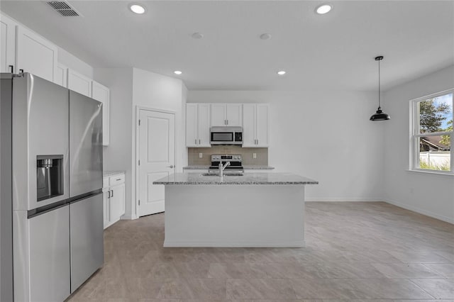 kitchen with decorative light fixtures, appliances with stainless steel finishes, light stone countertops, white cabinetry, and a kitchen island with sink