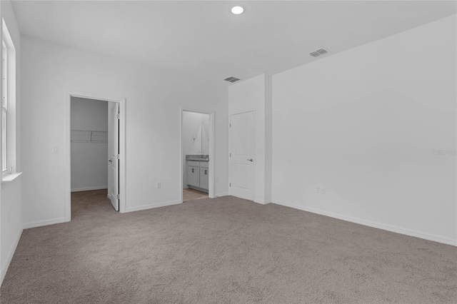 unfurnished bedroom featuring ensuite bathroom, a spacious closet, light colored carpet, and a closet