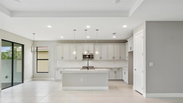 kitchen with a kitchen island with sink, light stone countertops, decorative light fixtures, and appliances with stainless steel finishes