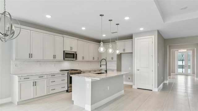 kitchen with backsplash, a kitchen island with sink, sink, appliances with stainless steel finishes, and light stone counters