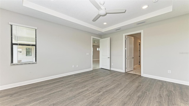 unfurnished bedroom with a textured ceiling, hardwood / wood-style flooring, ceiling fan, and a tray ceiling