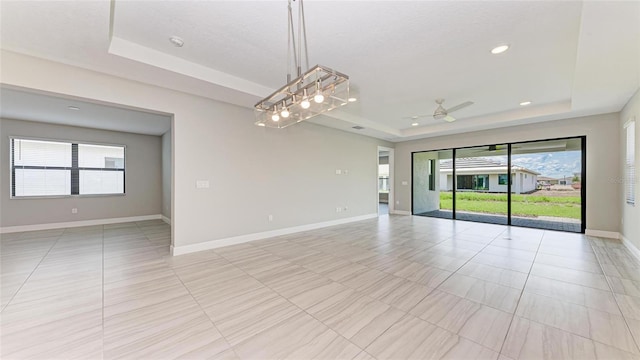 empty room featuring ceiling fan, a wealth of natural light, and a tray ceiling