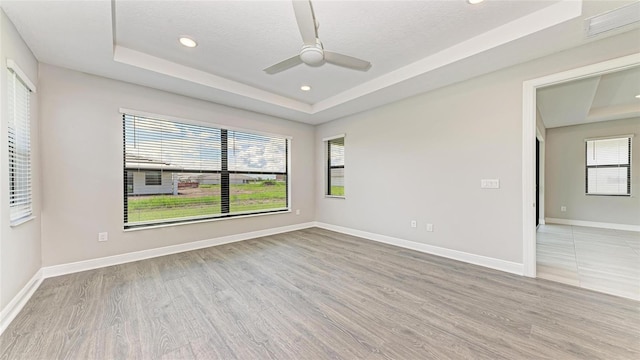 empty room featuring a raised ceiling, ceiling fan, a textured ceiling, and light wood-type flooring