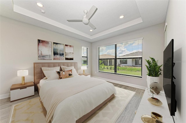 bedroom featuring a tray ceiling, ceiling fan, a textured ceiling, and light wood-type flooring