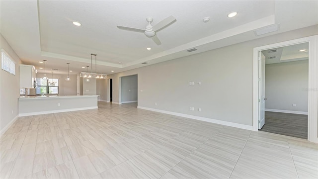 unfurnished living room featuring ceiling fan and a tray ceiling