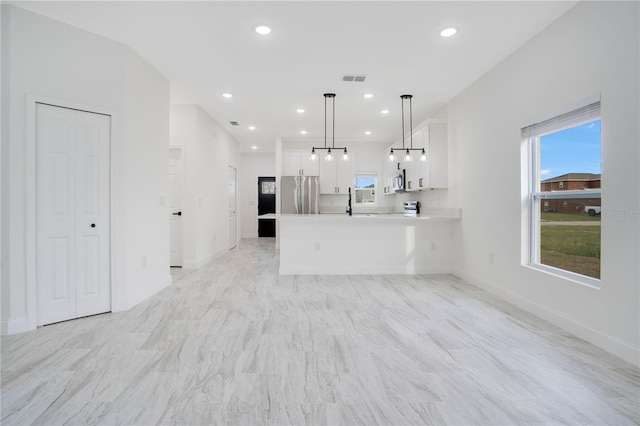 kitchen with kitchen peninsula, stainless steel fridge, a healthy amount of sunlight, hanging light fixtures, and white cabinetry