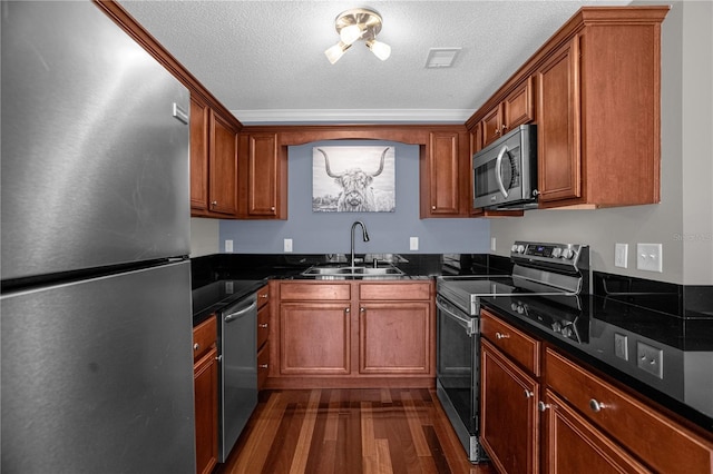 kitchen featuring a textured ceiling, appliances with stainless steel finishes, dark hardwood / wood-style flooring, dark stone countertops, and sink