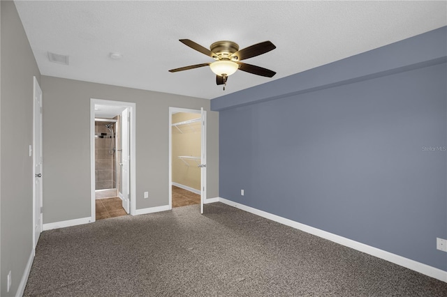 unfurnished bedroom with a closet, a spacious closet, dark colored carpet, and ceiling fan