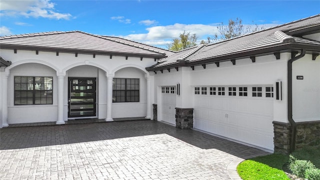 exterior space with a garage, stone siding, a tile roof, and decorative driveway