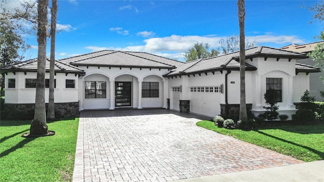 mediterranean / spanish house featuring a garage, stone siding, a tiled roof, decorative driveway, and a front lawn