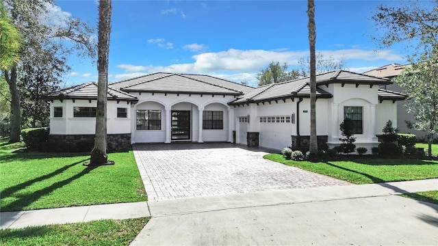 mediterranean / spanish-style house with a garage, a tiled roof, decorative driveway, a front yard, and stucco siding