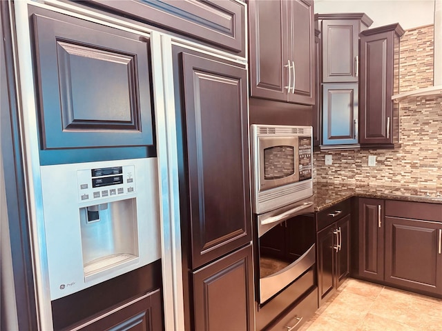 kitchen featuring light tile patterned floors, stainless steel appliances, backsplash, dark stone counters, and wall chimney exhaust hood