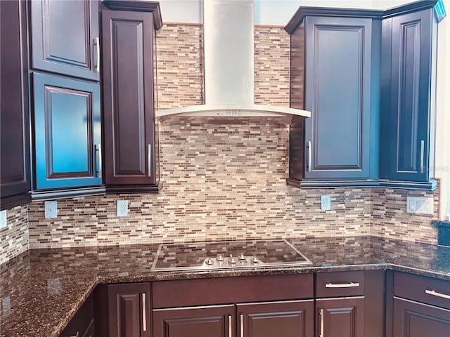 kitchen with stovetop, backsplash, wall chimney exhaust hood, and dark stone counters