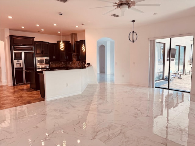 kitchen featuring decorative light fixtures, built in appliances, decorative backsplash, kitchen peninsula, and ceiling fan