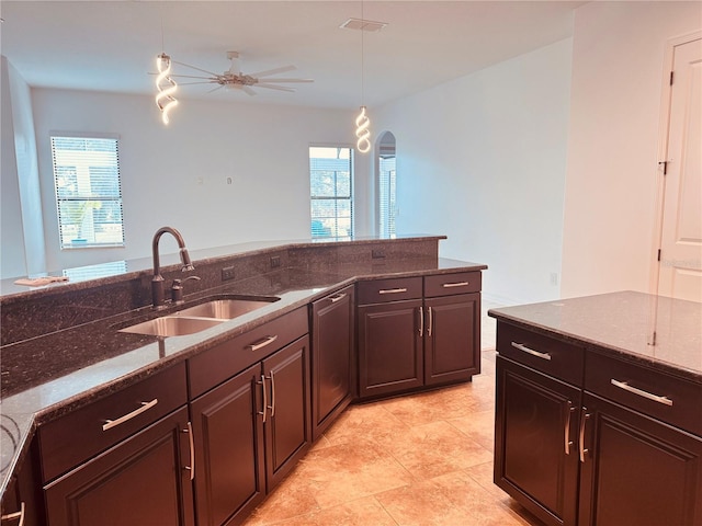 kitchen featuring visible vents, hanging light fixtures, a ceiling fan, a sink, and dark stone counters