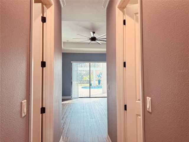 corridor featuring a textured wall, baseboards, and wood finished floors