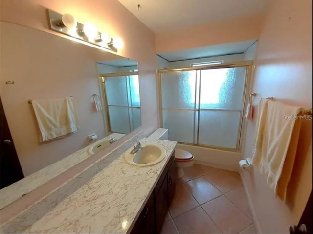 full bathroom featuring toilet, tile floors, bath / shower combo with glass door, and vanity with extensive cabinet space