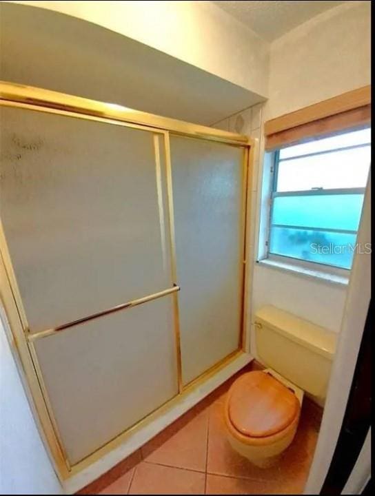 bathroom featuring an enclosed shower, toilet, and tile flooring