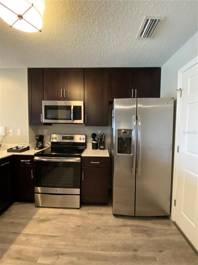 kitchen featuring appliances with stainless steel finishes, a textured ceiling, dark brown cabinetry, and light wood-type flooring