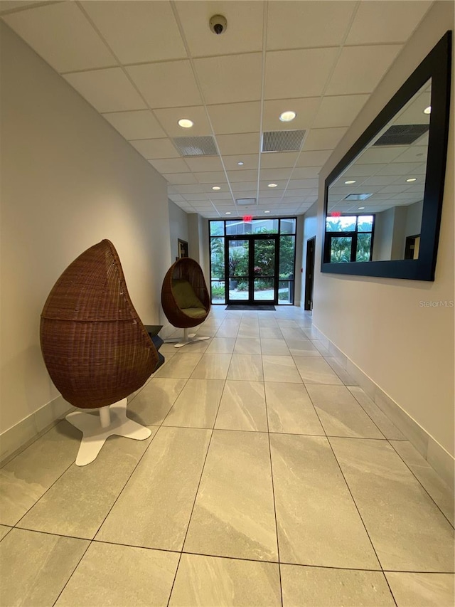 hallway featuring floor to ceiling windows, light tile floors, and a drop ceiling