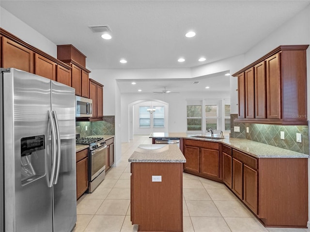 kitchen with ceiling fan, sink, light stone countertops, kitchen peninsula, and appliances with stainless steel finishes