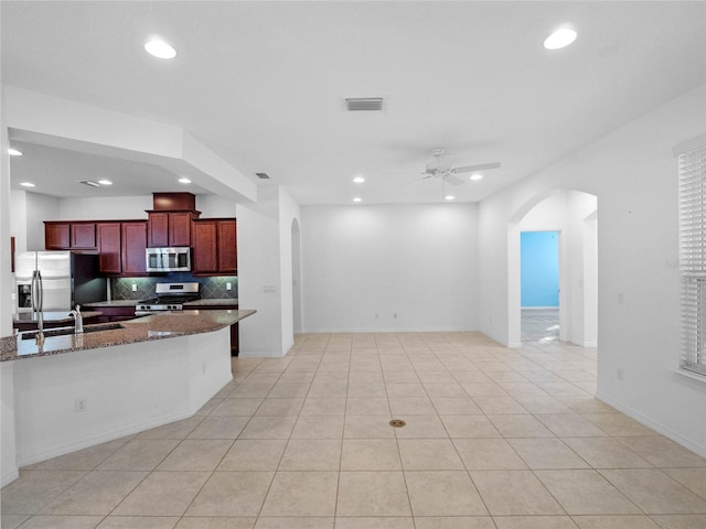 kitchen featuring ceiling fan, dark stone counters, decorative backsplash, light tile patterned flooring, and appliances with stainless steel finishes