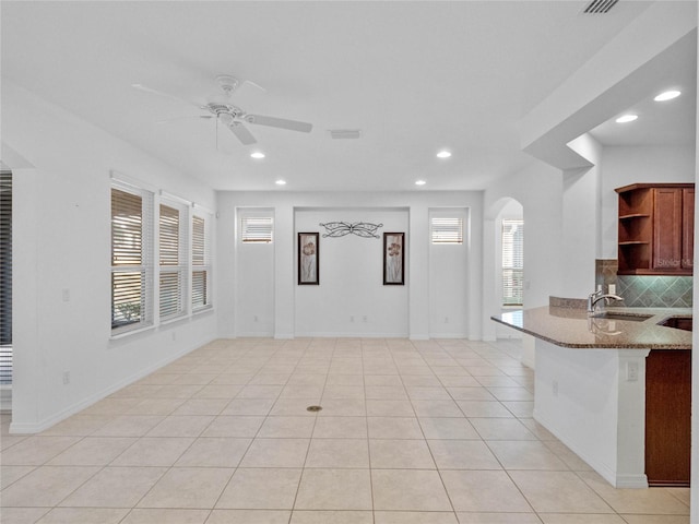 interior space featuring light stone countertops, kitchen peninsula, backsplash, ceiling fan, and light tile patterned flooring